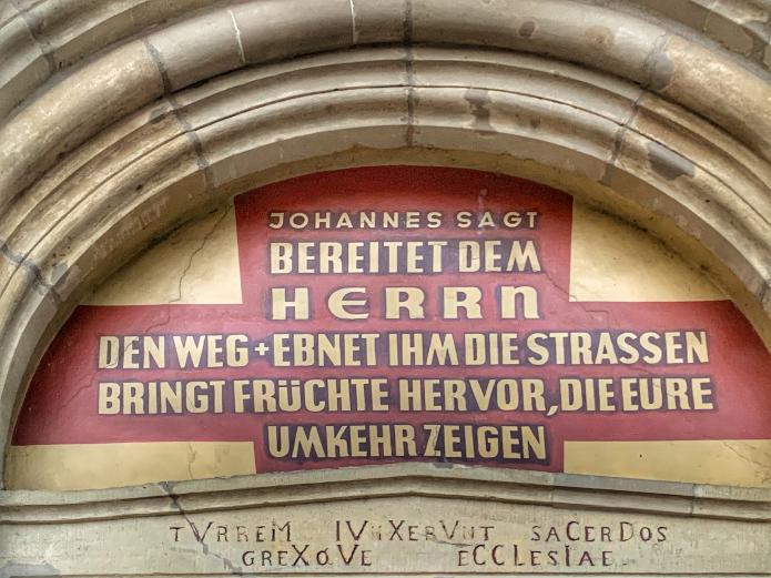 Eine Botschaft von Johannes dem Täufer begrüßt die Menschen über dem Portal von St. Johann Baptist. Foto: © Elvis Katticaren / Stadtdekanat Köln